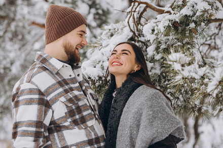 A young happy and loving couple is standing under a pine tree fr, a Holiday Photo by Cherkas Photography