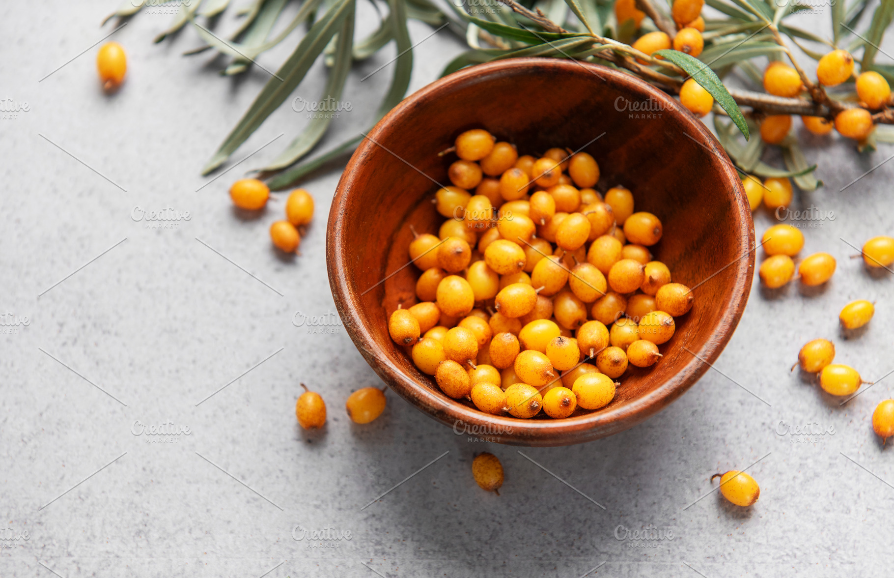 Sea buckthorn berries in wooden bowl on grey background, a Food & Drink Photo by Olena Rudo