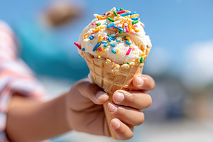 Melting ice cream cone held by child with colorful sprinkles on a sunny day, a Food & Drink Photo by AlyaAnd