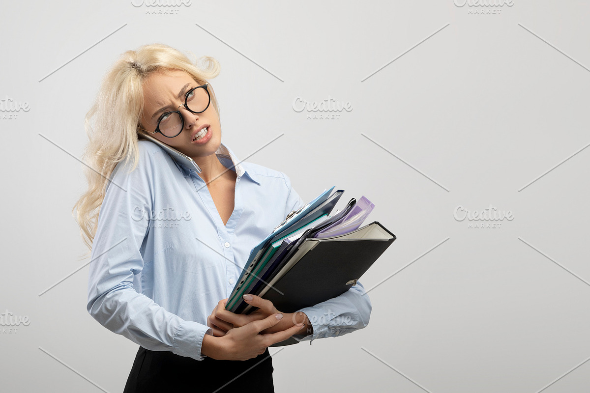 Stressed female office worker with heap of papers talking on smartphone on ligh, a Photo by Prostock-Studio (Photo 2 of 2)