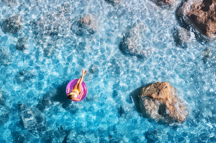 Aerial view of a young woman swimming with swim ring in blue sea, a Holiday Photo by den-belitsky