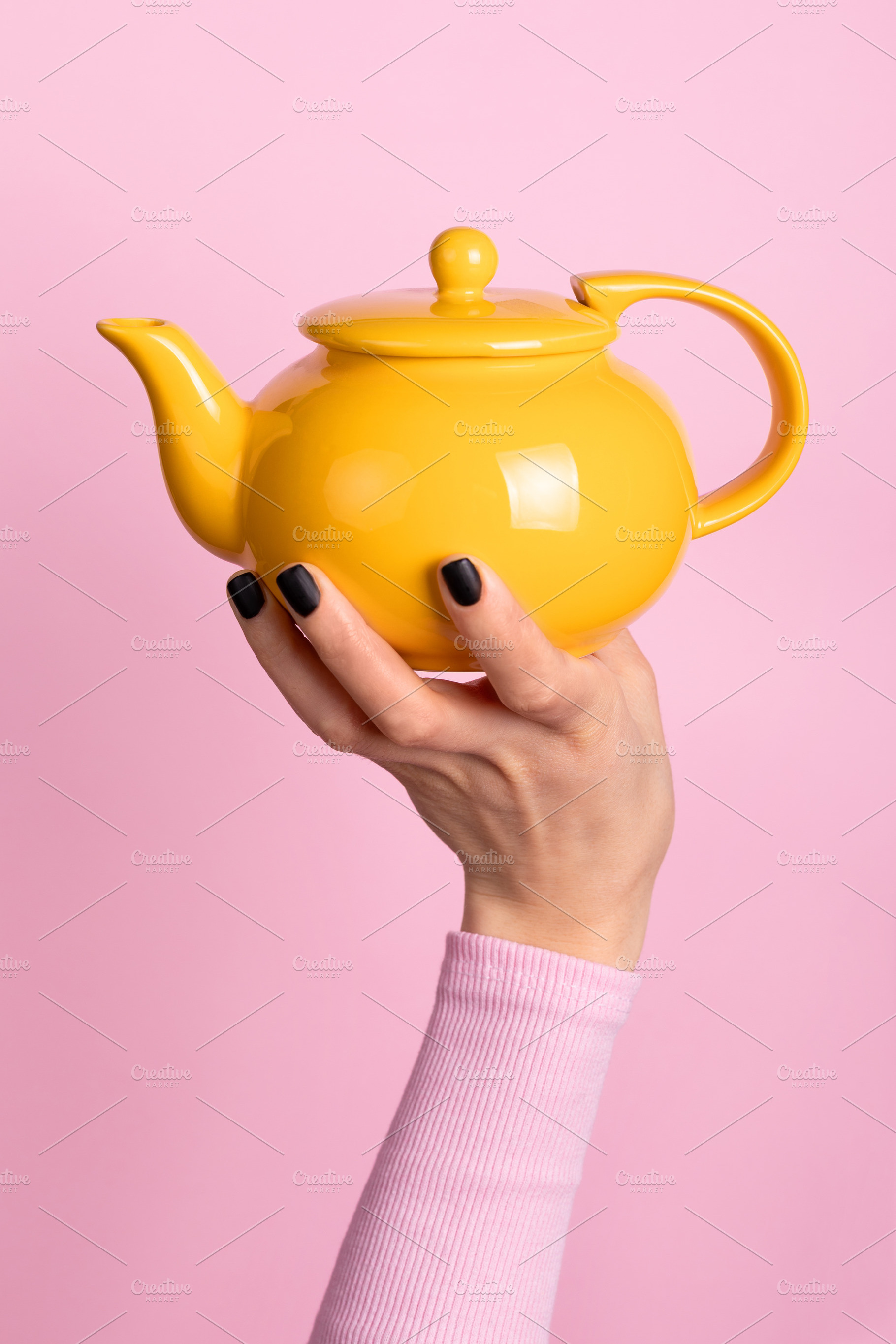 Hand holding a vibrant yellow teapot against a pastel pink backg, a Nature Photo by Ales Munt