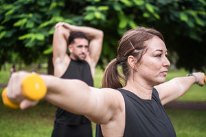 Woman lifting dumbbells during outdoor strength training with male partner
