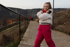 Cheerful young girl in a white jacket and pink pants standing on, a Person Photo by Ales Munt