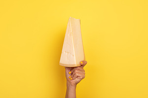 Hand with yellow nails holding a large wedge of cheese raised a, a Food & Drink Photo by Ales Munt
