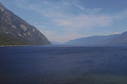Lake Teletskoye between mountains with blue clear sky in Altai, a Nature Photo by TravelFlow