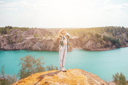 Beautiful girl on the top of the rock with blue lake on background, a Person Photo by travnikovstudio