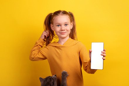 Smiling girl in mustard sweater holding smartphone with blank sc