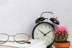 Eyeglasses resting on stack of notebooks with pen, alarm clock,, a Background Photo by Olena Rudo