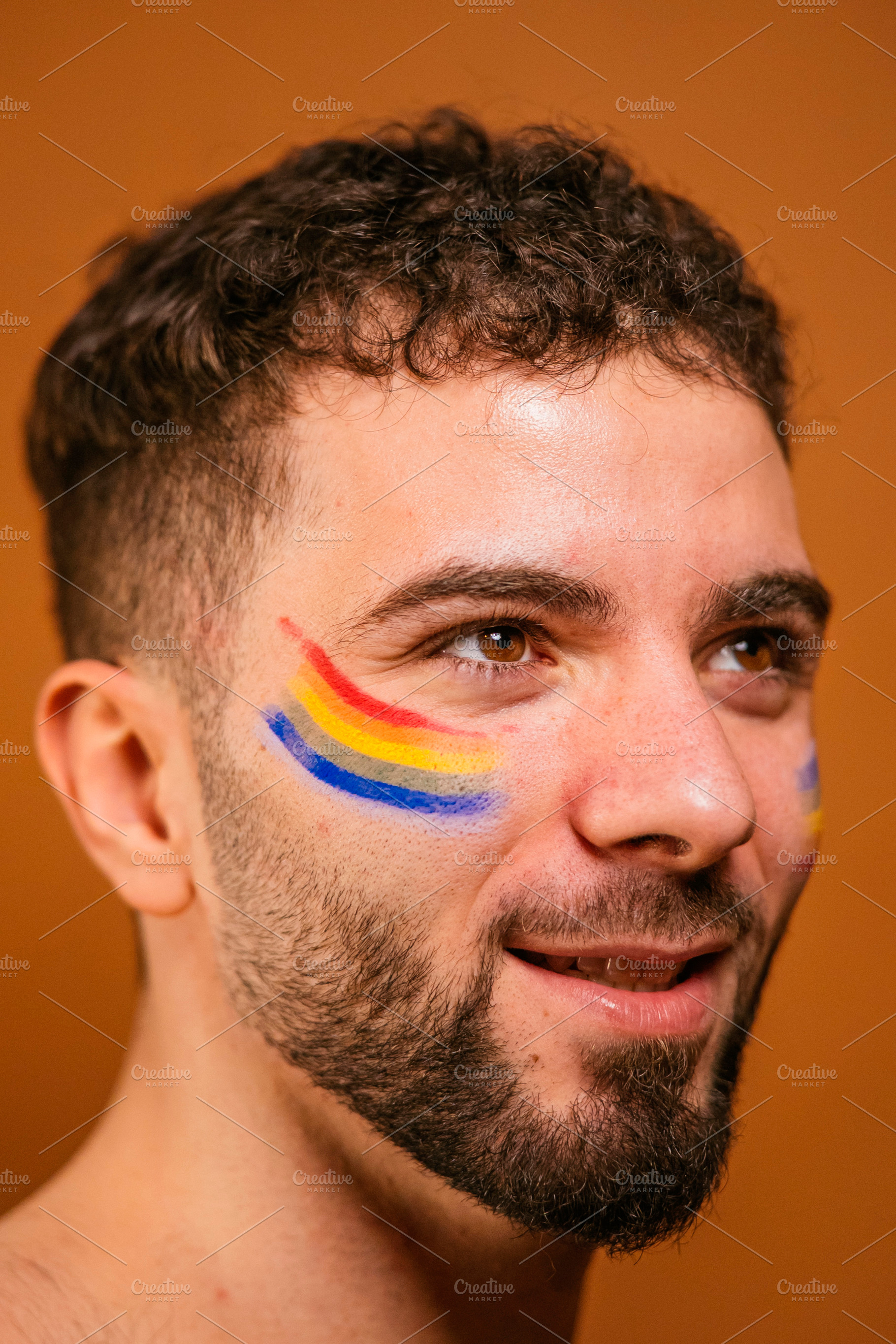 Young man with rainbow face paint celebrating pride, a Photo by karrastock