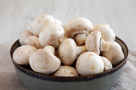 Raw White Champignon Mushrooms in a Bowl on a white wooden backg, a Food & Drink Photo by LiudmylaChuhunova