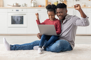 Emotional black father and daughter using laptop together at home, a Photo by Prostock-Studio