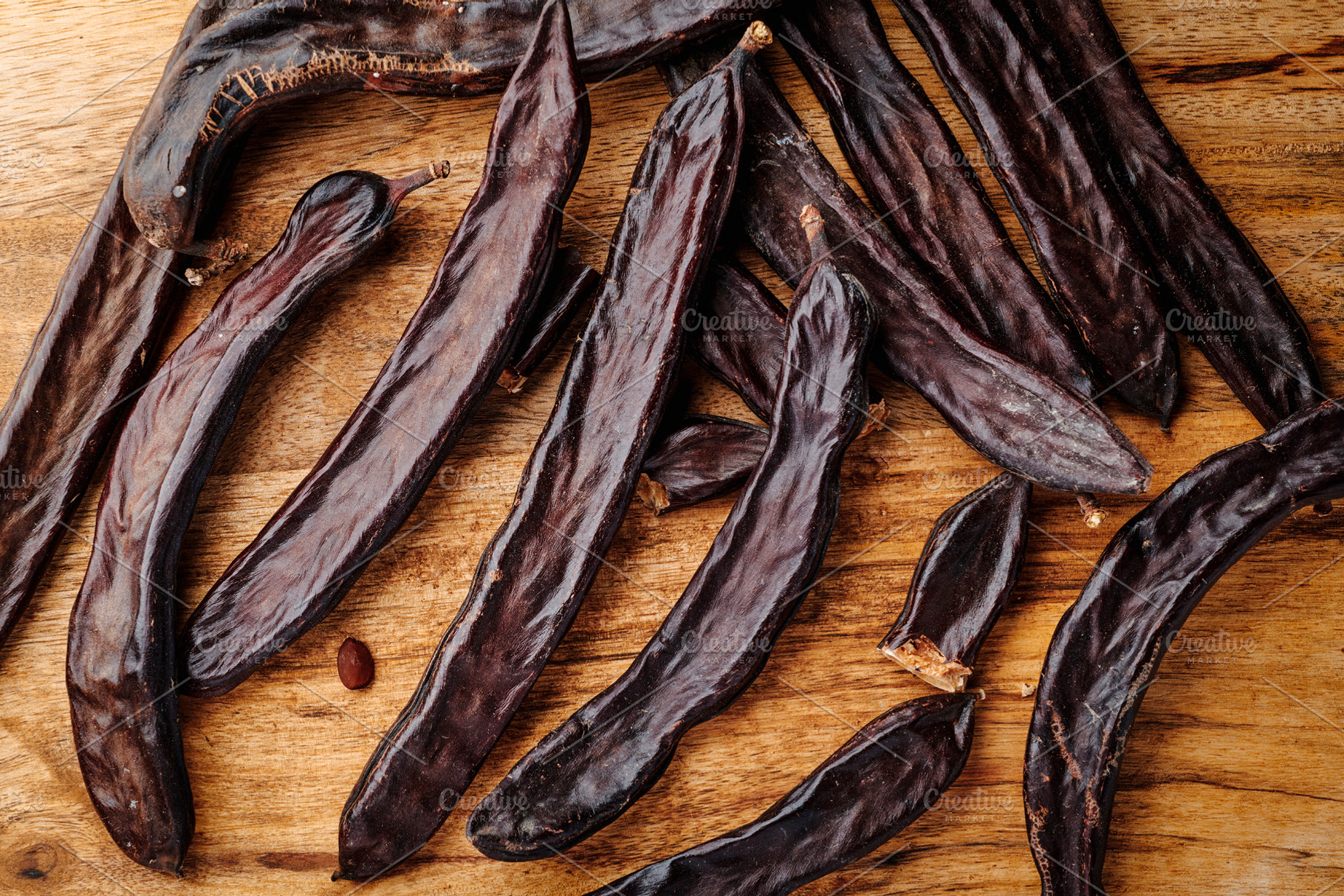 a group of ripe carob pods on a wooden table, a Photo by Nito