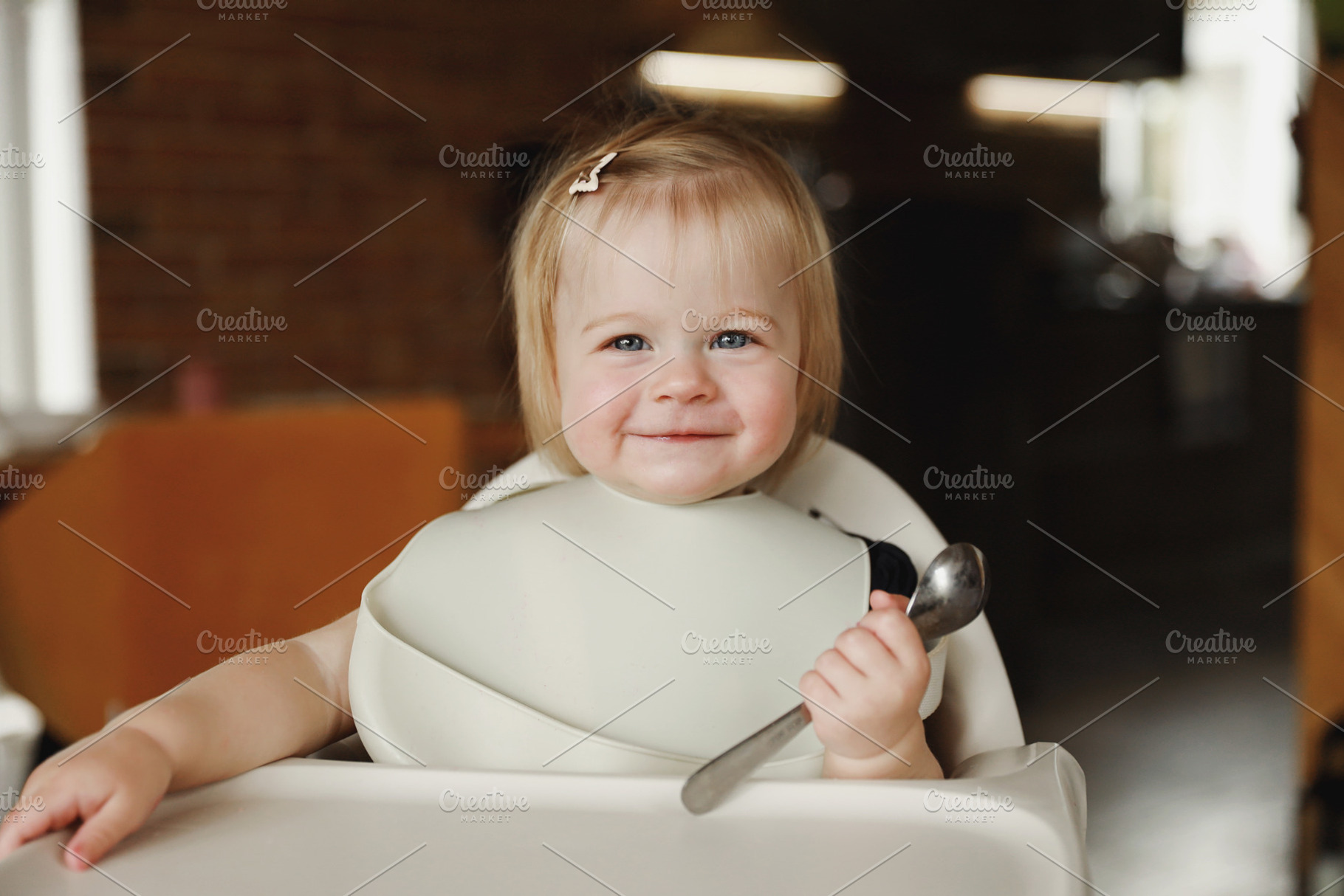 Infant girl or toddler sitting on high chair. Eating food by herself using spoo, a Person Photo by Lenor4ik