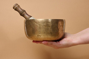 A copper singing bowl and a wooden mallet in a woman's hand