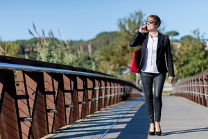Businesswoman walking on bridge talking on phone, a Photo by RF Images