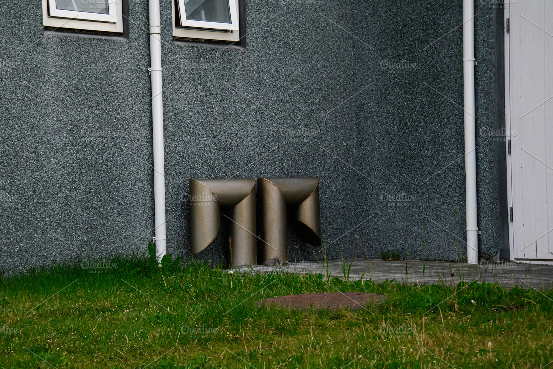 Metallic ventilation pipes outside a grey building in Akranes, surrounded by gr, a Photo by AS photostudio