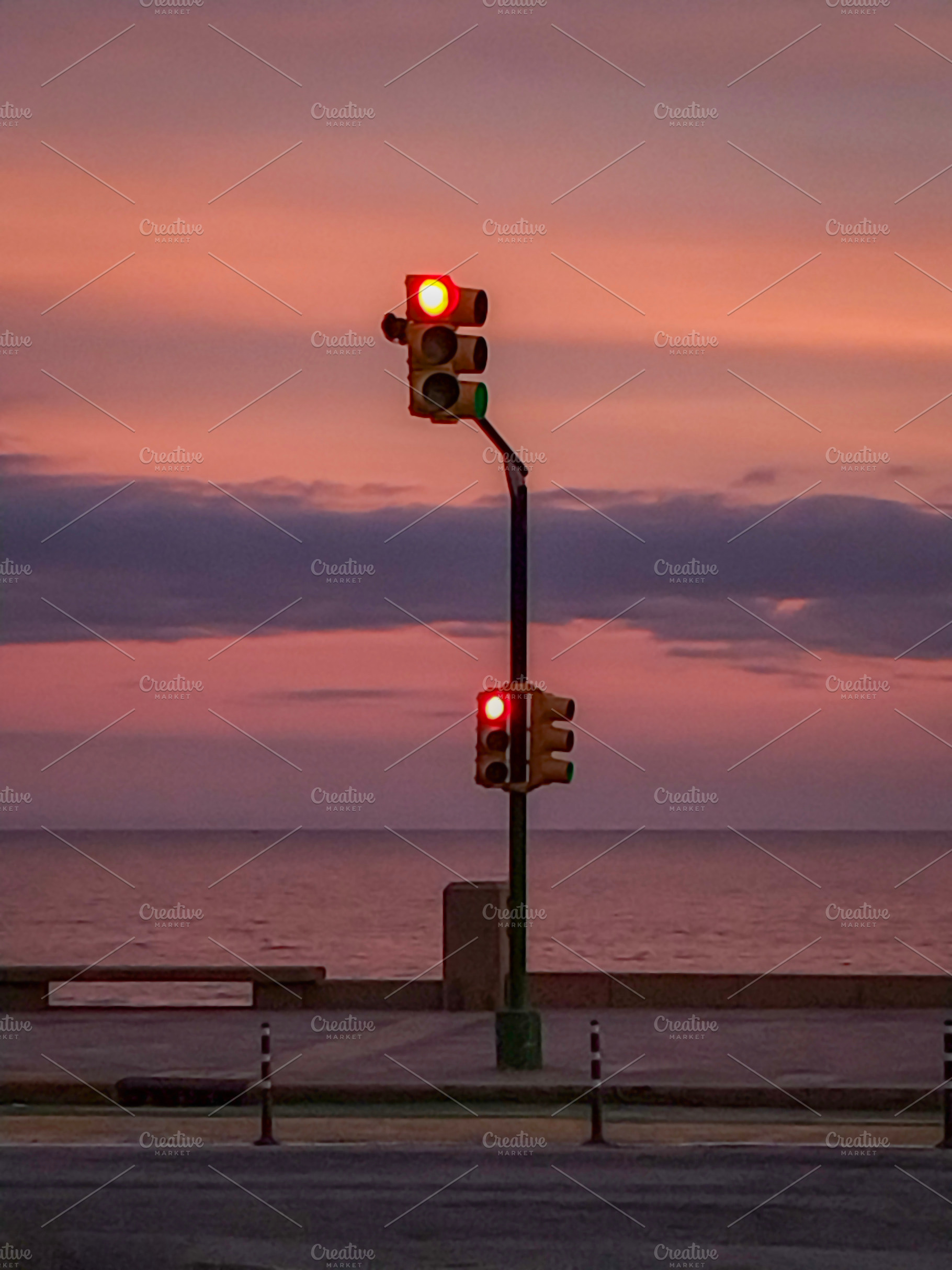 Traffic light glowing at sunset by the sea, a Transportation Photo by DanFLCreativo