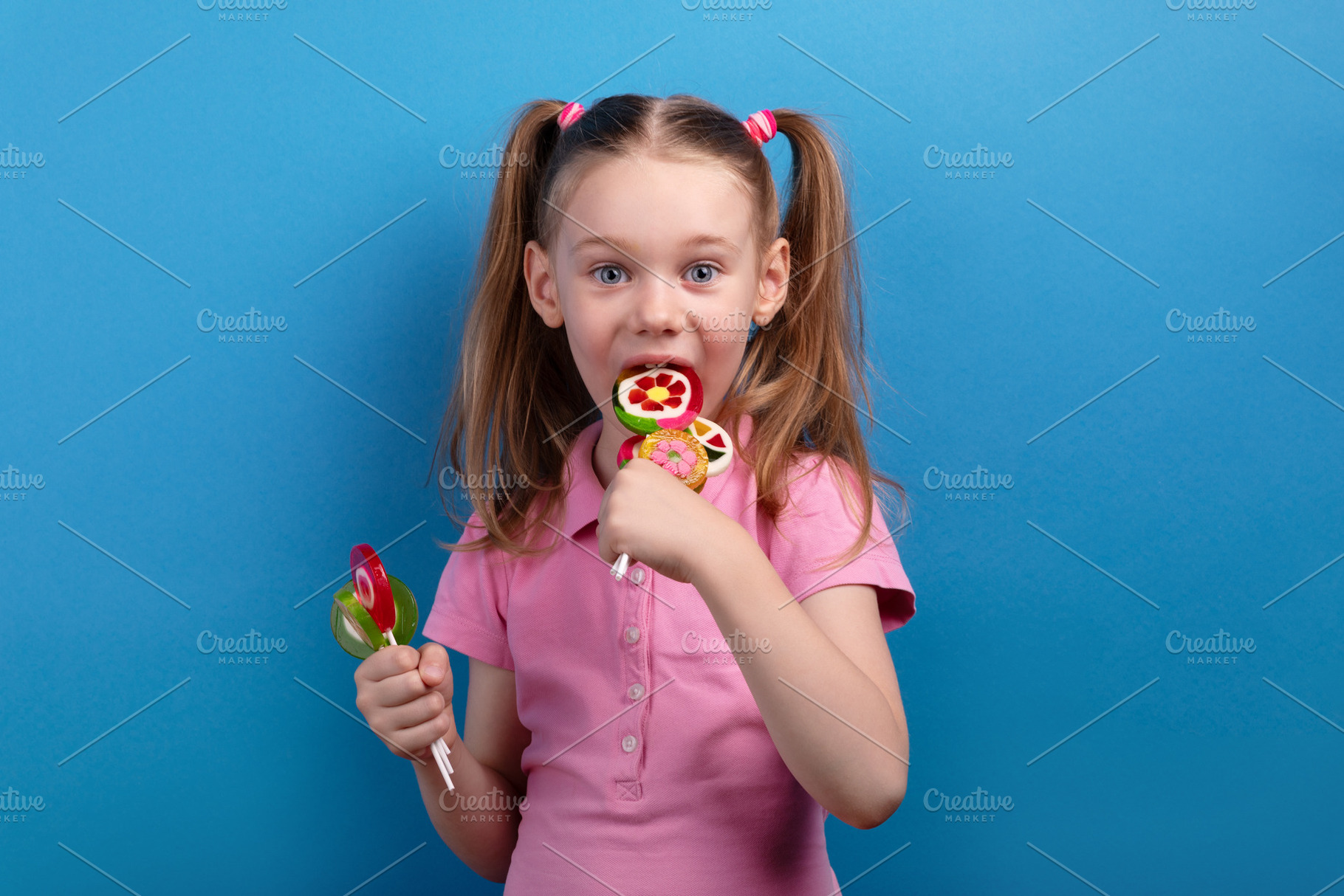 Excited young girl in a pink shirt biting into colorful fruit-sh, a Person Photo by Ales Munt