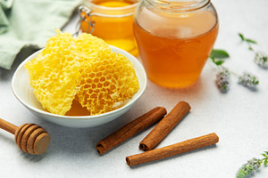 Honeycomb, honey jar, cinnamon sticks, and honey dipper resting, a Food & Drink Photo by Olena Rudo