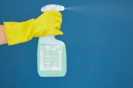 Hand, spray and detergent for cleaning, hygiene or anti bacteria chemical against a blue studio background. Hands of glove spraying liquid bottle for washing, clean sanitary or disinfection on mockup, a Photo by Peopleimages.com