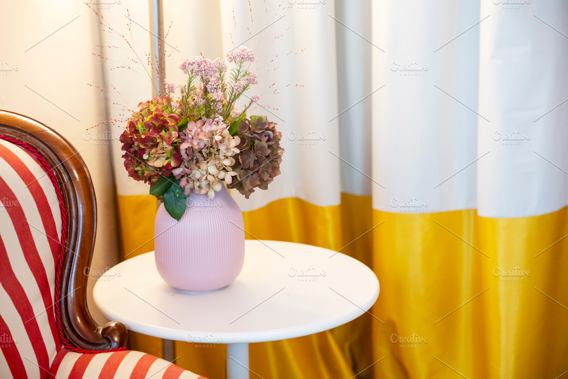 Flower arrangement in a pink vase on a white side table next to, an Architecture Photo by Imaginarium