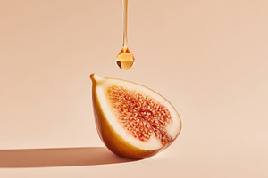 Sliced fig with honey drop on peach background, a Food & Drink Photo by AlyaAnd