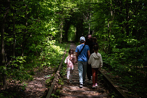 Family walking on abandoned railway tracks in a verdant green forest, a Photo by AS photostudio