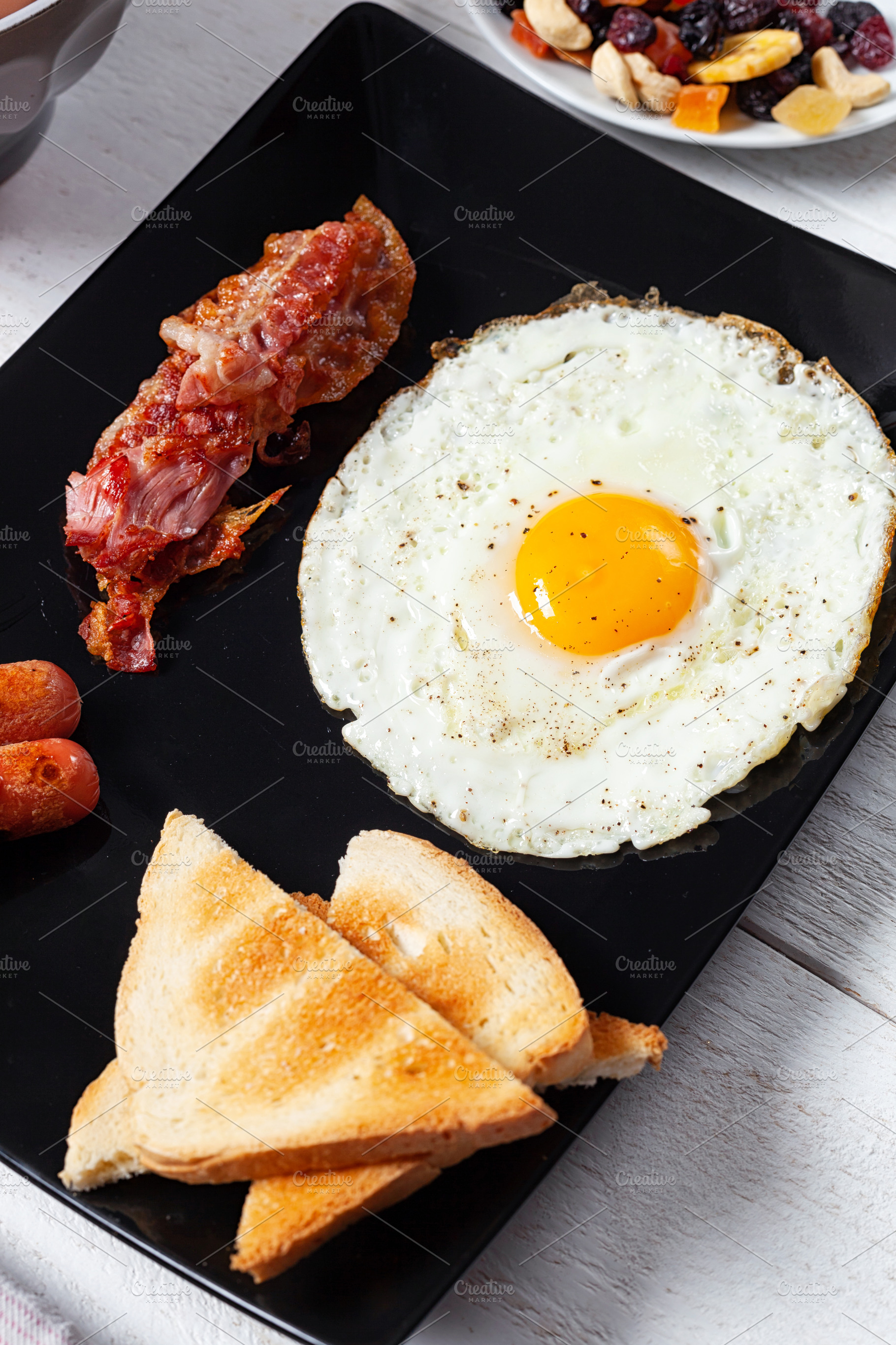 Delicious full English breakfast with fried egg, bacon, sausages and toast on b, a Food & Drink Photo by Antonio Gravante Market