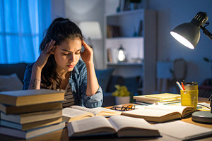 Stressed student surrounded by books and papers at bedroom, a Person Photo by DanFLCreativo