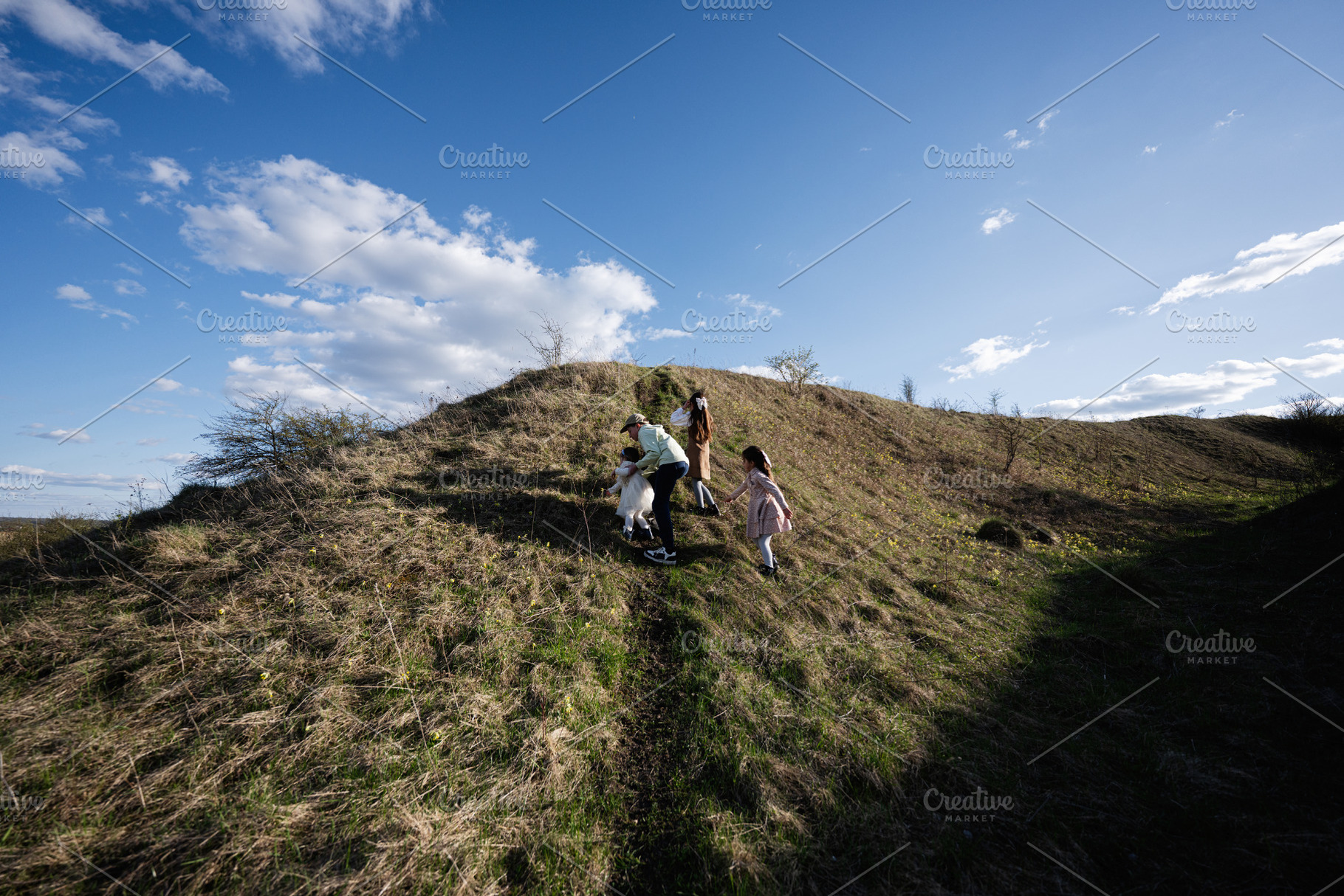 Family of children climbing a grassy hill on a sunny day enjoying outdoor play, a Person Photo by AS photostudio