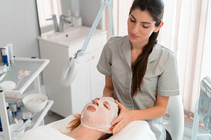 Massage therapist applying hydrating face mask to woman at salon, a Photo by andreonegin market