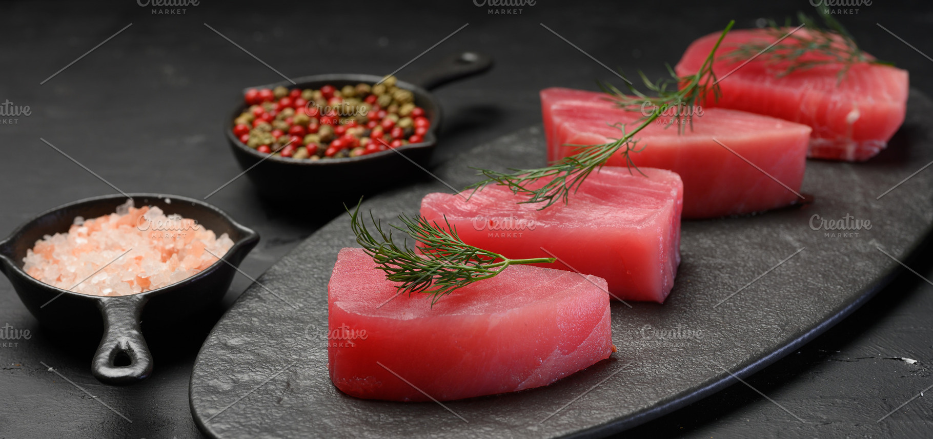 Raw tuna pieces on a black board, decorated with dill sprigs, a Food & Drink Photo by ndanko