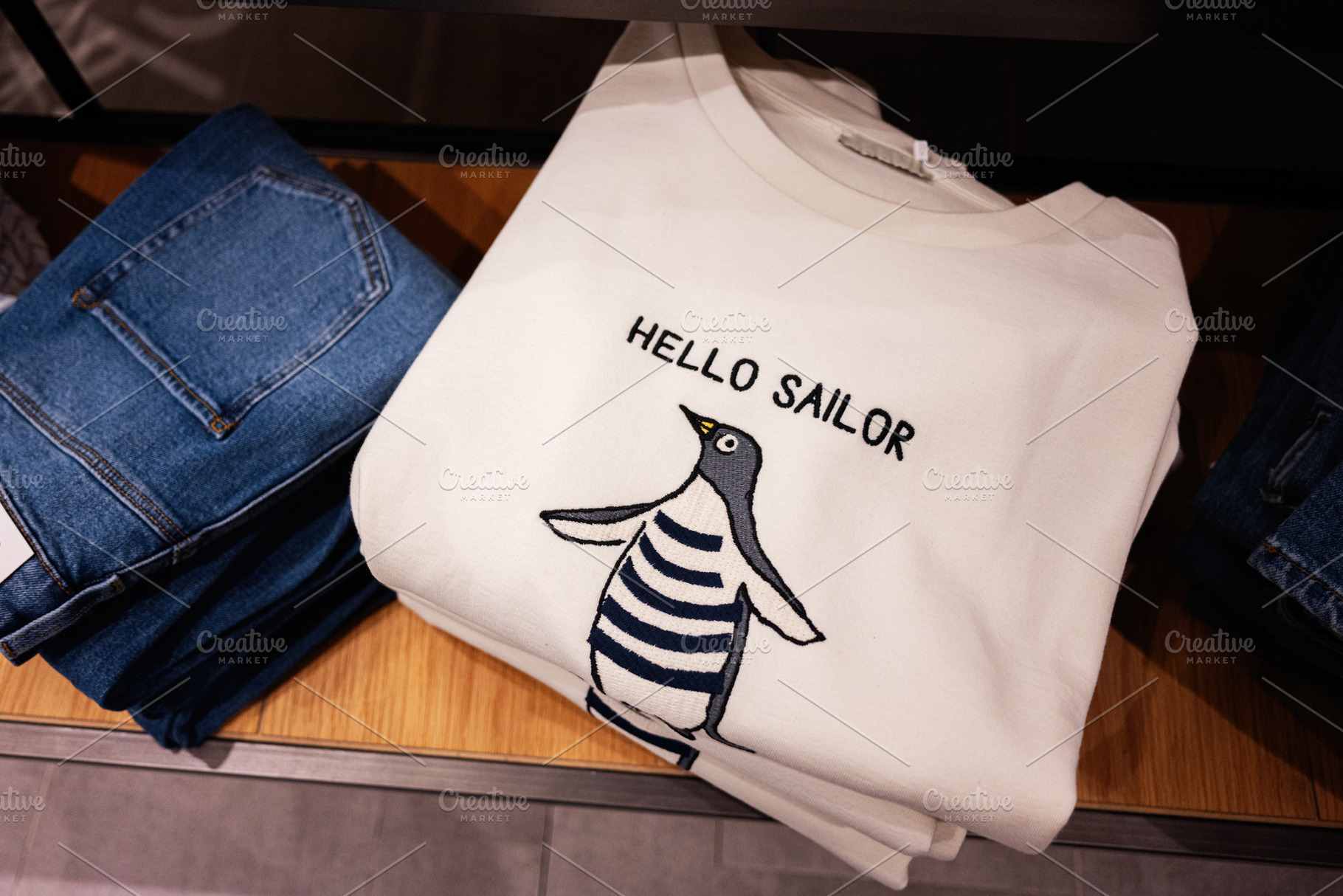 Folded white sweater with penguin design and text alongside blue denim jeans, a Photo by AS photostudio