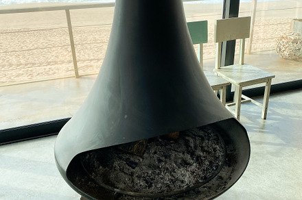 Modern fireplace with ash and logs, framed by ocean waves visibl