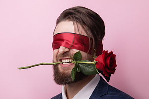 Bearded man in a suit wearing a red blindfold, biting a red rose, a Person Photo by Ales Munt