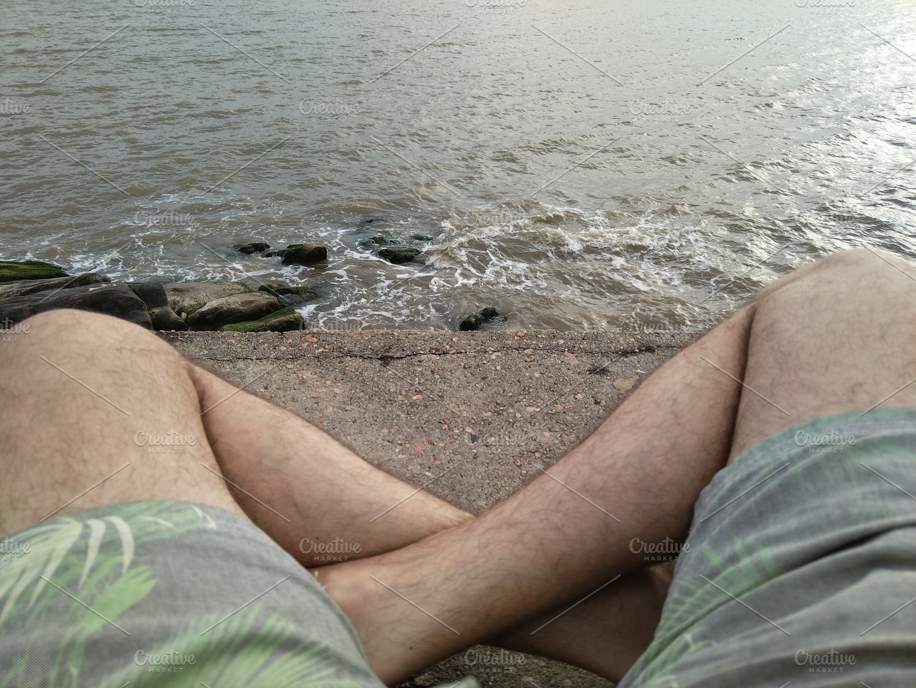 Person sitting by water with legs visible and  shorts, a Person Photo by DanFLCreativo