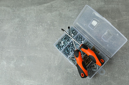 Box with screws and screwdrivers on gray textured background, an Industrial Photo by AtlasStudio PRO