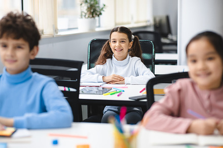 Portrait of small girl sitting at desk in classroom, a Photo by Prostock-Studio