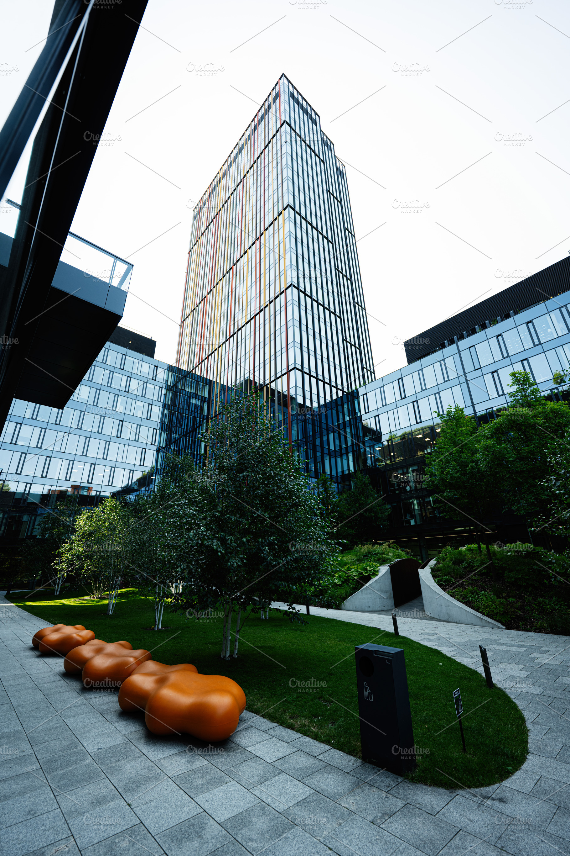 Modern glass building with landscaped green area and orange seating features, a Photo by AS photostudio
