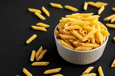 Organic Dry Penne Pasta in a Bowl on a black background, side vi, a Food & Drink Photo by LiudmylaChuhunova