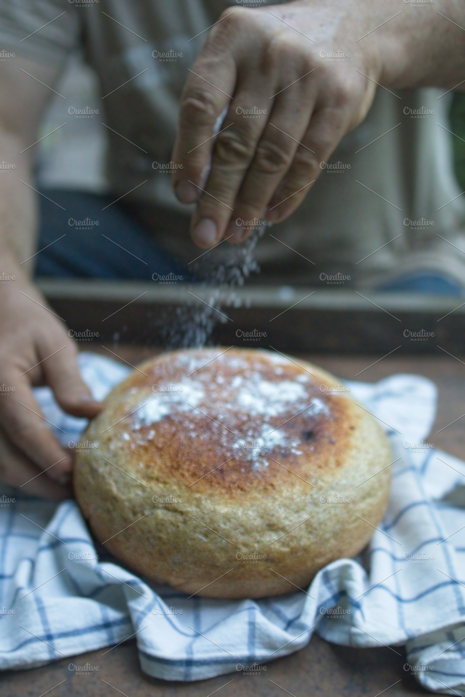 Baker's hand sprinkles flour on fresh bread close-up. A man finishes baking, de, a Food & Drink Photo by TanaCh