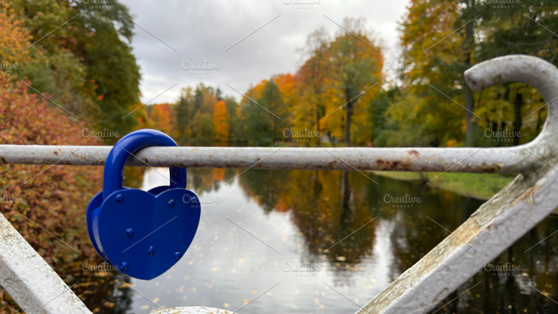 A blue heart-shaped padlock on a metal railing by a river with autumn trees., an Industrial Photo by Textures & Backgrounds
