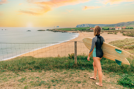 Surfer woman with wetsuit and surfboard looking at the beach, a Holiday Photo by davidpereiras