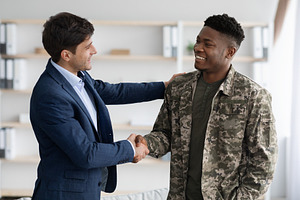 Cheerful guy in suit shaking black military man hand, a Photo by Prostock-Studio