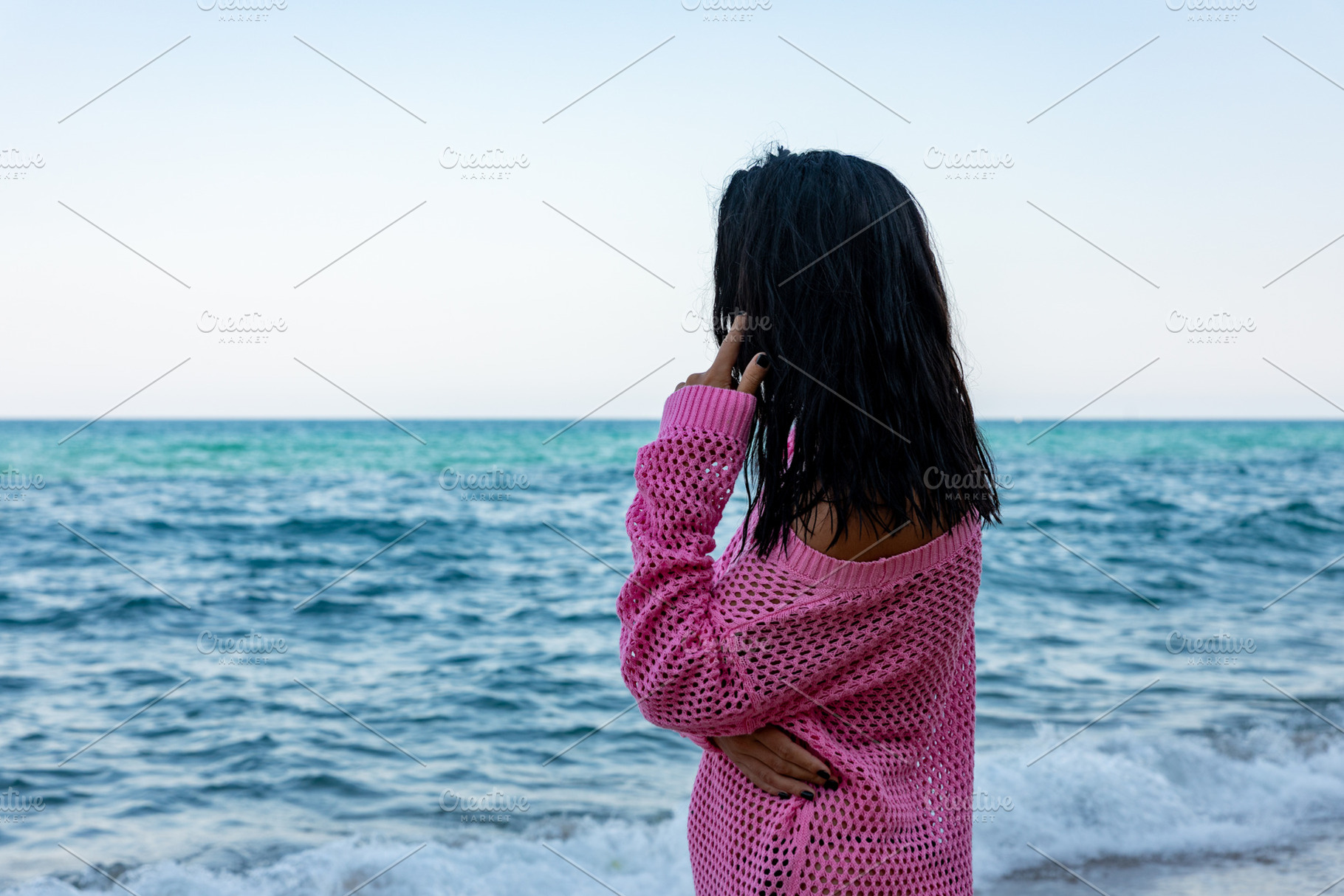 Woman in a pink sweater stands by the sea, gazing at the waves. Serene beach sc, a Holiday Photo by Ales Munt