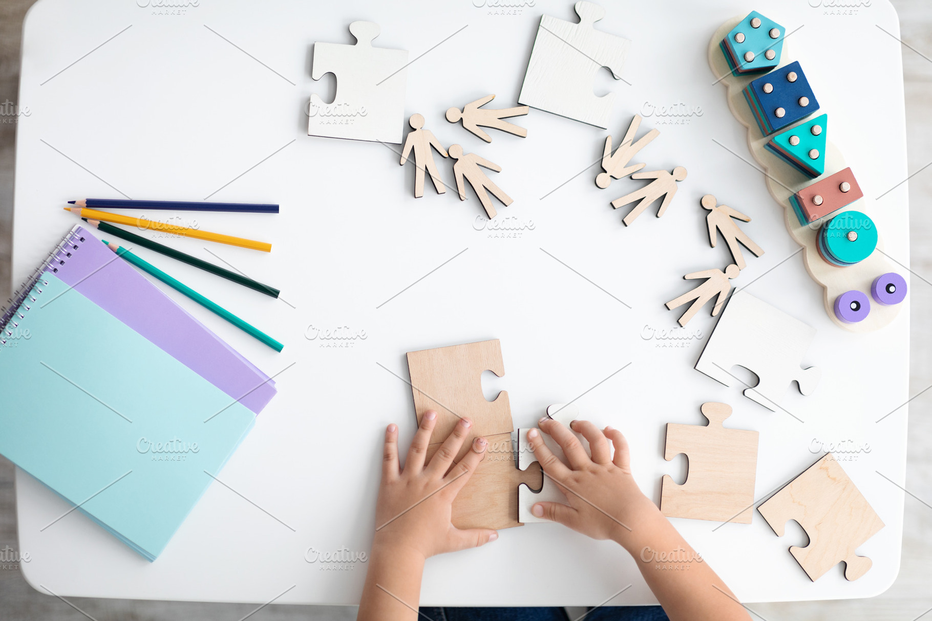 Unrecognizable little kid playing with wooden puzzles pieces on desk, top view,, a Photo by Prostock-Studio