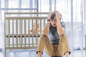 Tired father sitting by baby crib at, a Person Photo by Elizaveta Galitskaya