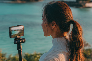 Woman filming scenic ocean view with, a Photo by Pixeness Studio