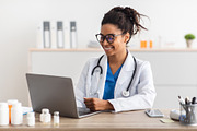 Portrait of smiling doctor looking at screen sitting at desk, a Photo by Prostock-Studio (Thumbnail 1 of 2)